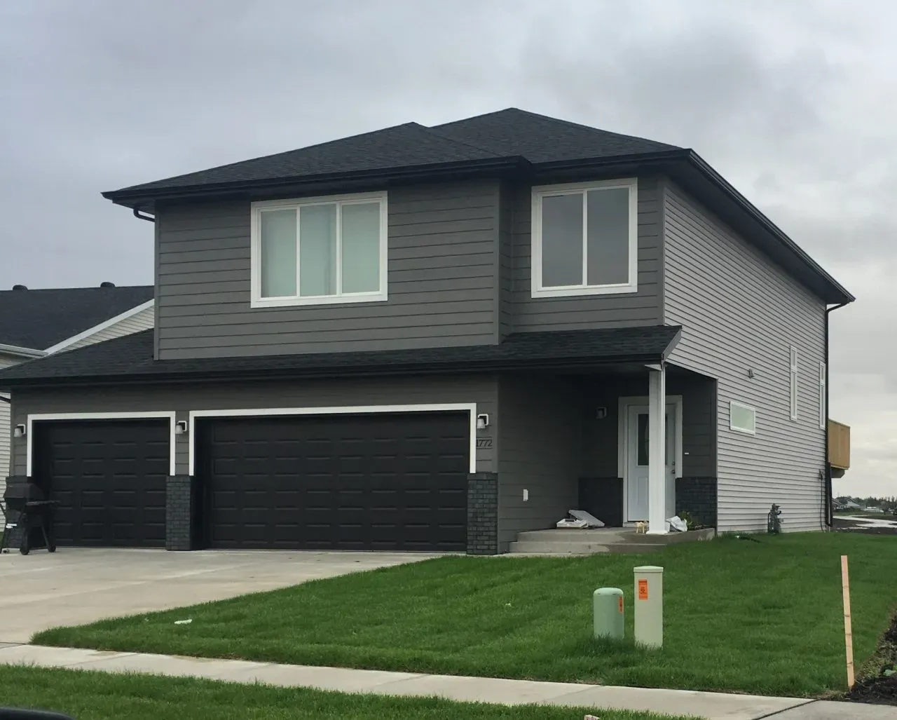 Two-story modern gray house with a double garage and a neatly trimmed lawn. Overcast sky in the background creates a calm and subdued atmosphere.